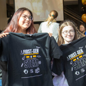 Two first generation STEM students hold up t-shirts