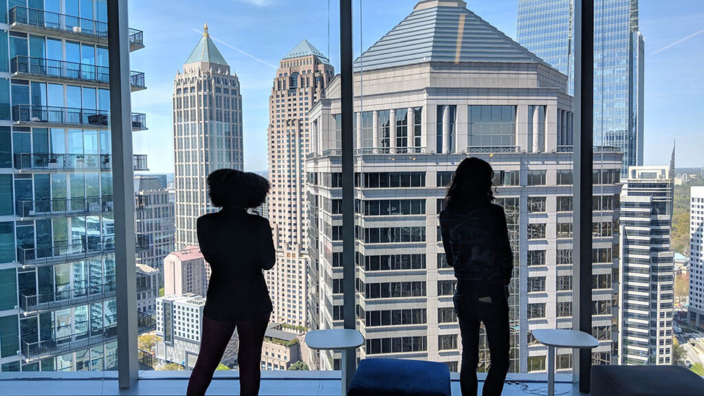 Two young professionals look out onto the Atlanta skyline from within a tall building.