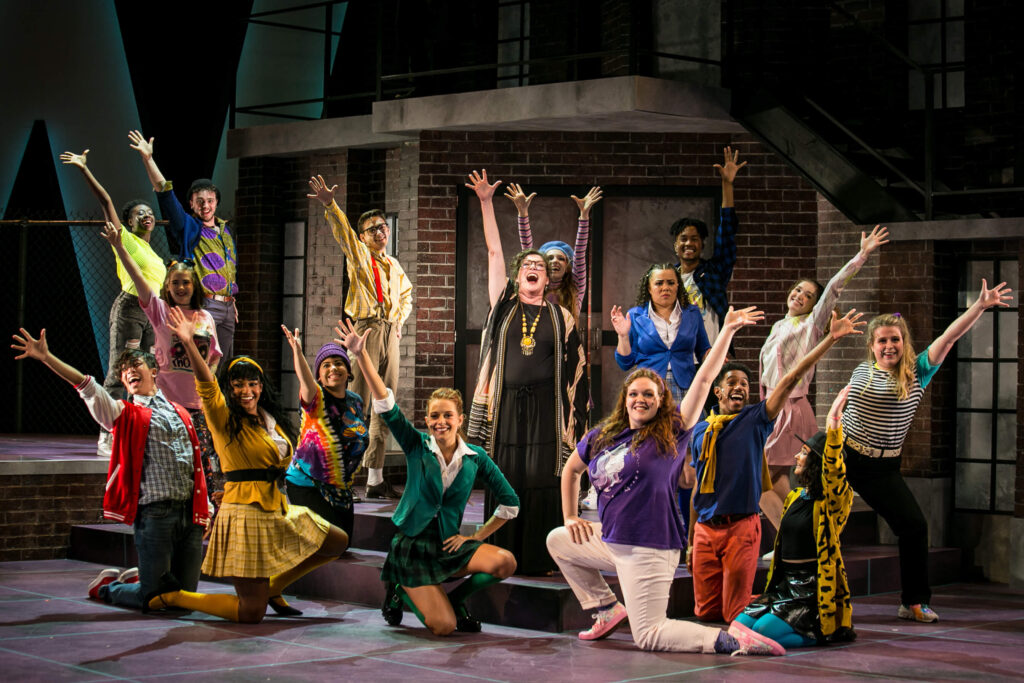 OU Theatre performers pose on stage, hands raised, during Heathers.