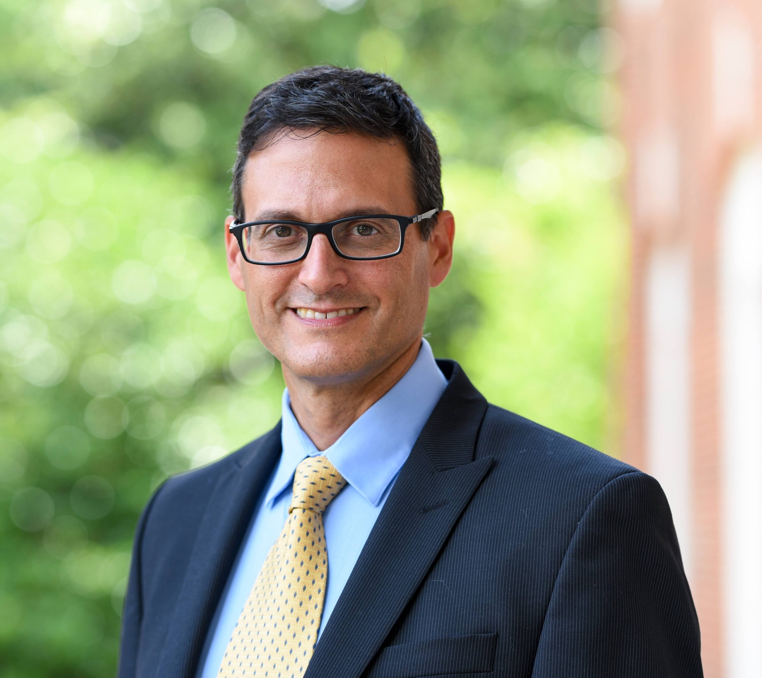 Man in a suit and tie with trees and a building in the background