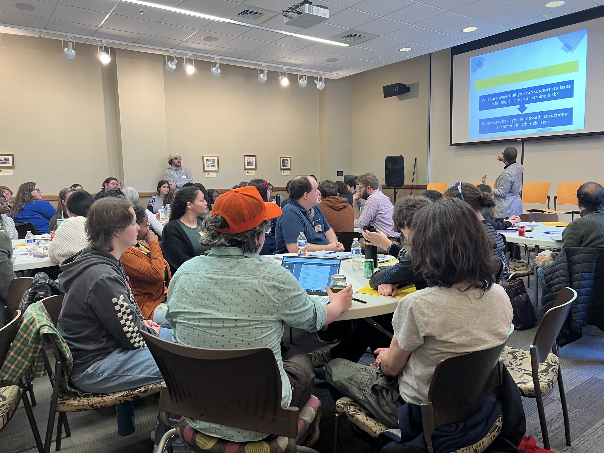 Tables of students and faculty listen to a presentation on peer instruction