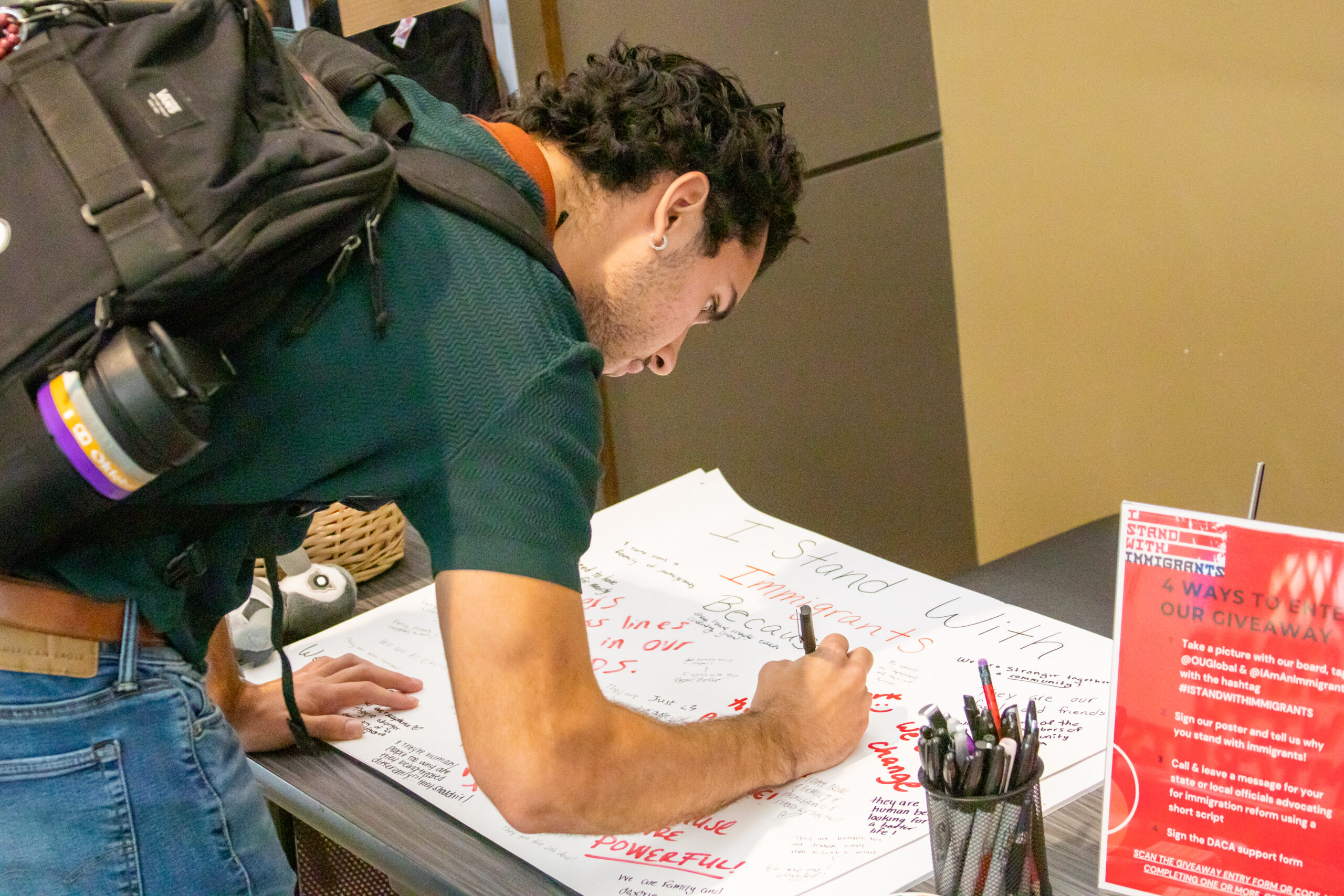 A student signs a poster in support of immigrants at the "I Stand with Immigrants" Day of Action event