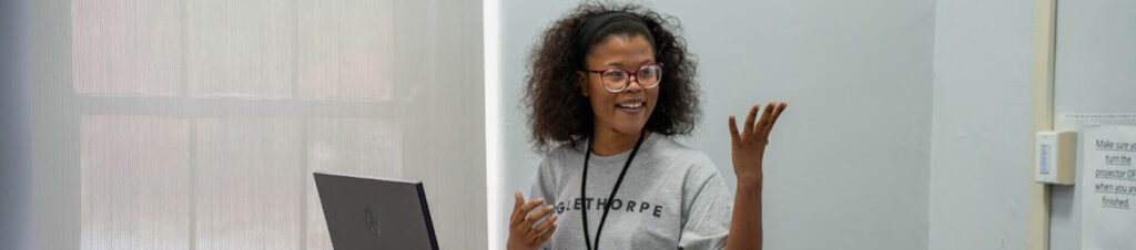 A student smiles what standing at a computer presenting in a classroom.