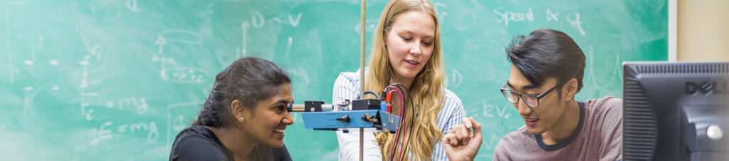 Physics students use lab equipment next to a computer.