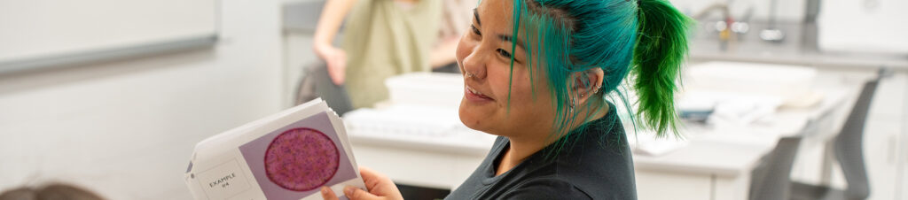 A student smiles while showing an image of a cell.