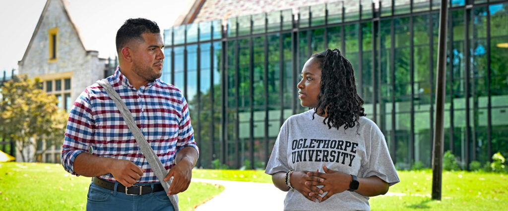 Two students walk along the sidewalk in front of Cousins Center on a sunny day.