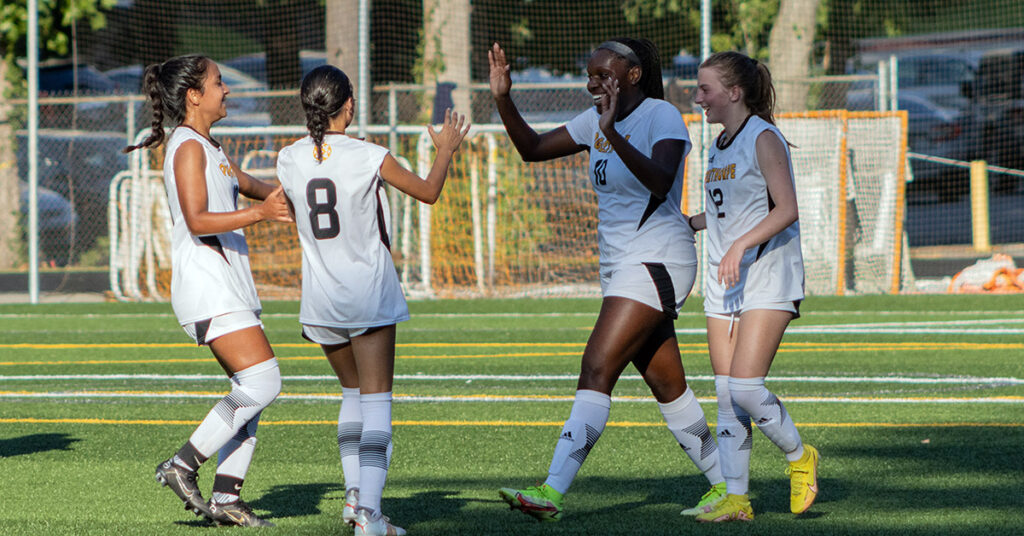 Womens Soccer team members high five on the field.