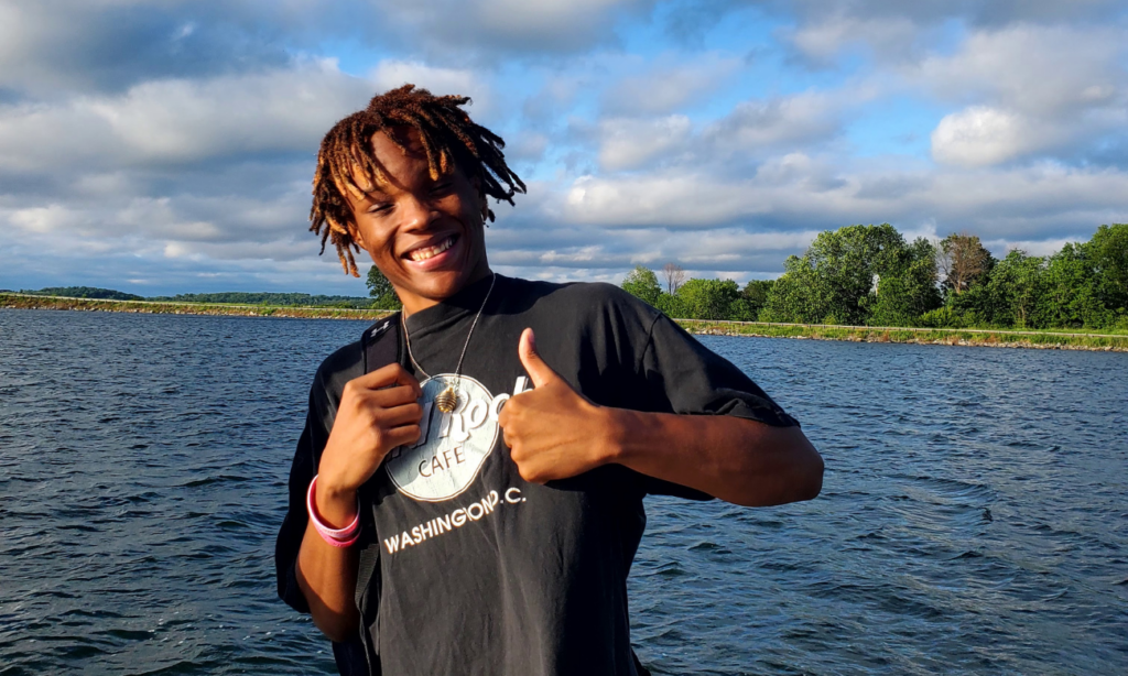 Caleb Murphy during his time with AmeriCorp poses in front of a lake with his thumb up.