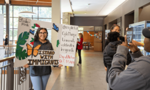 Student poses with a large photo frame that reads "I stand with immigrants."