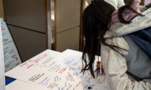 Student writing a message on a poster board in support of immigrants.