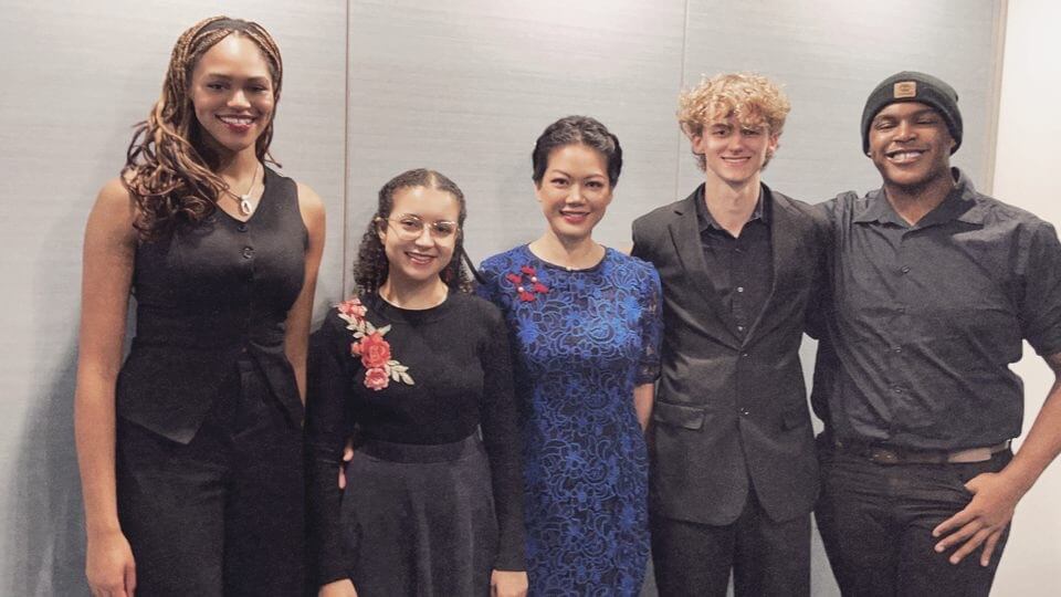 Singers dressed in black pose for a photo with event attendee. From left to right: Isabella Reid '28, Adarys Encarnacion '26, event attendee, Carter Daniels, Nehemiah Wiggins '27.