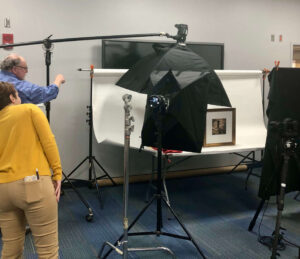 Two speakers doing a presentation on photographing an exhibit with camera equipment and white backdrop.