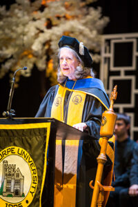 Dr. McClymond speaks from a podium in her academic regalia.