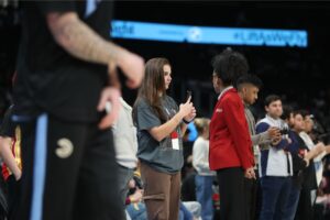 A woman with a cell phone stands on the sideline.