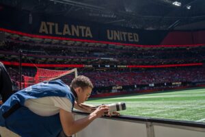 A student prepares to take a photo on the sidelines of a soccer game