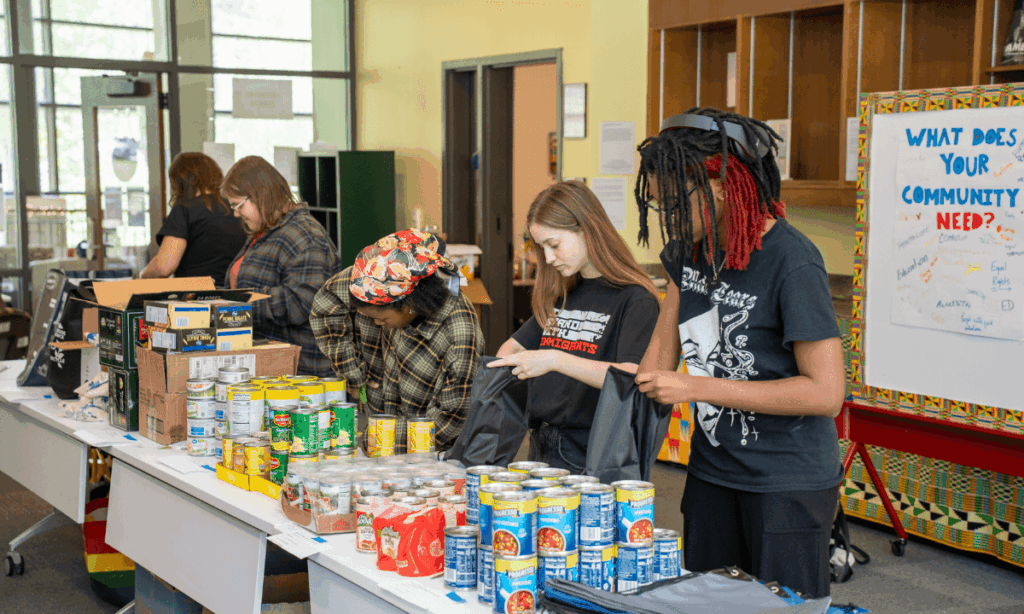 Students working in an assembly line to pack drawstring bags with canned goods for APS students.