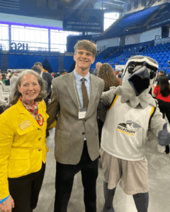 Austin Alman wears a gray suit and poses for a photo with President McClymond and Petey.