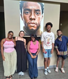 Oglethorpe University Museum of Art student docents pose in front of a portrait of Chadwick Boseman.