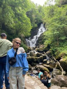 Tatum McBride wears sunglasses and poses in front of waterfall.