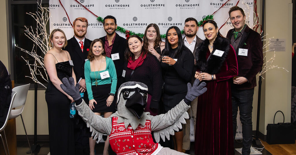 Petey in a holiday sweater poses with a group of Alumni at Boar's Head 2024.