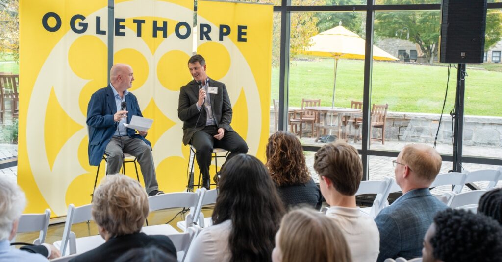 Two speakers in front of a large banner that says "Oglethorpe" speak to a crowd