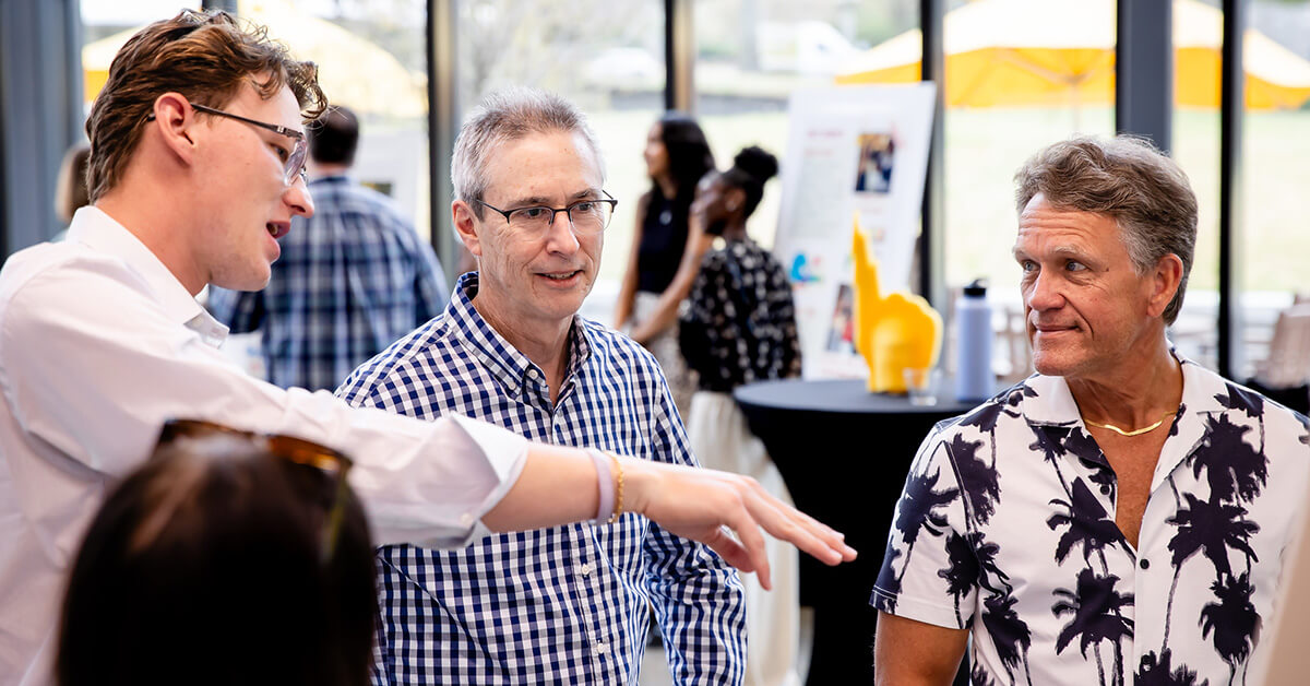A student presents at Alumni Weekend to two alumni in Co