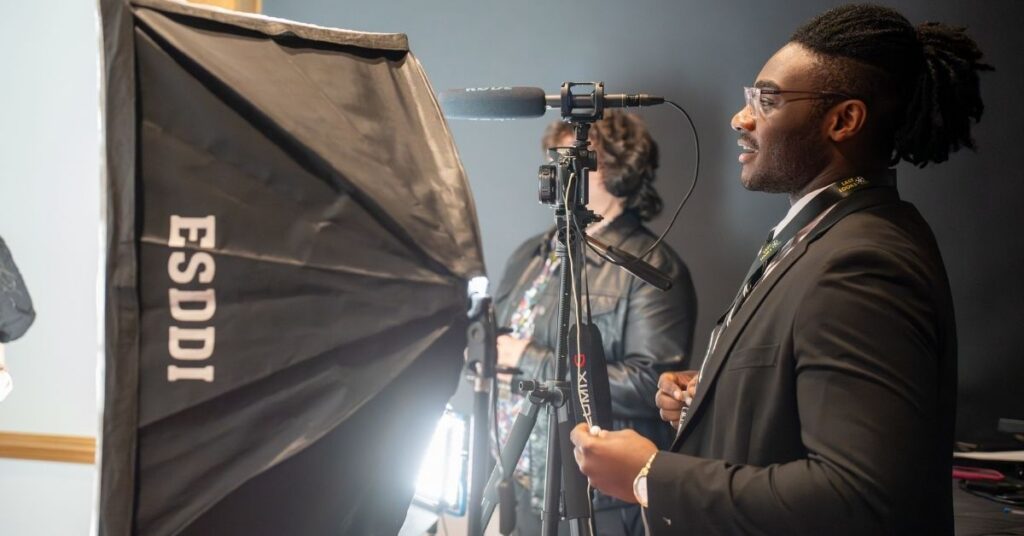 A student in a suit next to a camera outfitted with a boom mic and a lightbox