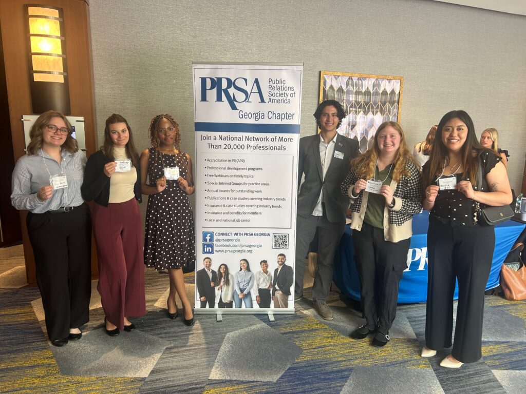 Students wearing business professional attire stand next to a pull up banner that says "PRSA Georgia Chapter."