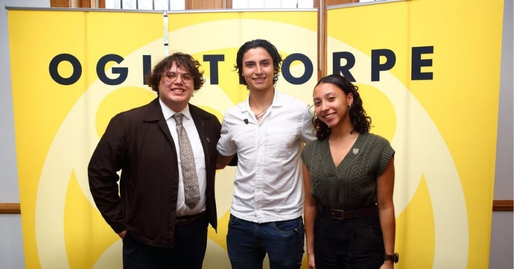 Three students pose in front of a yellow backdrop with "Oglethorpe" on it.