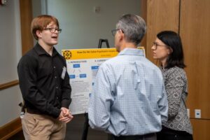 A student in front of a research poster speaks to two people about their project