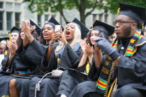 Graduates cheering and clapping facing the commencement stage.