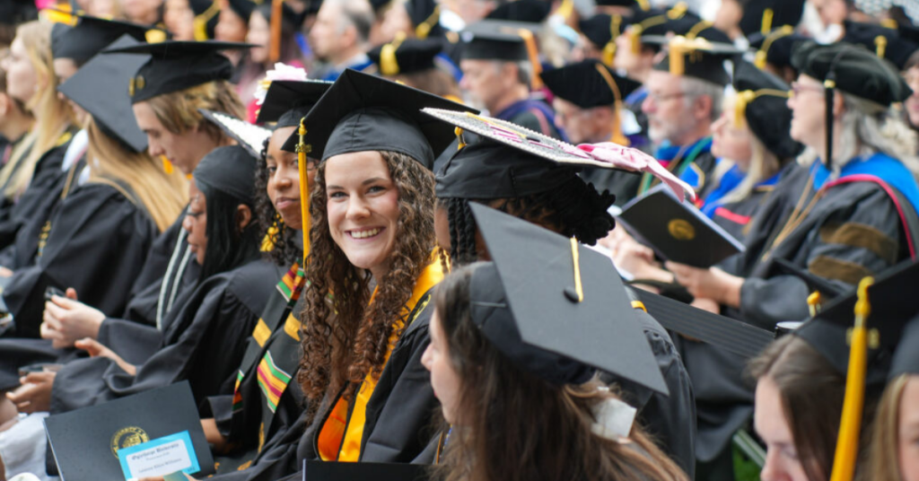 Graduate smiles brightly seated amongst other Oglethorpe graduates.