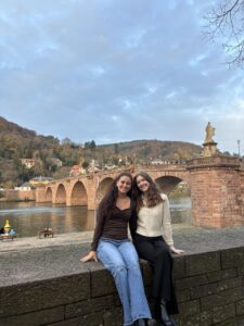 Two women sit in front of a bridge.