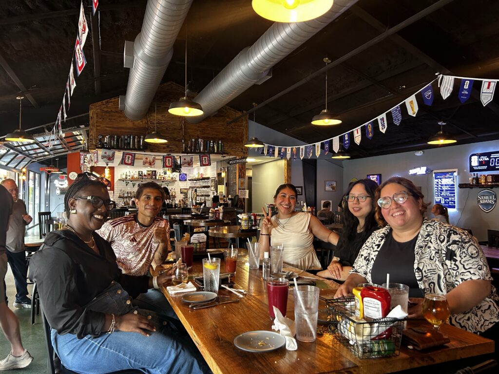 Group of people sitting around a table with drinks and plates of food.