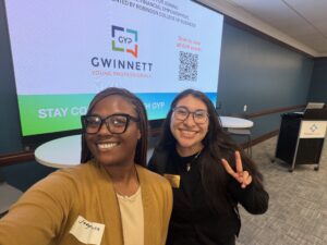 Two women in business casual attire pose in front of a screen that says "Gwinnett Young Professionals."