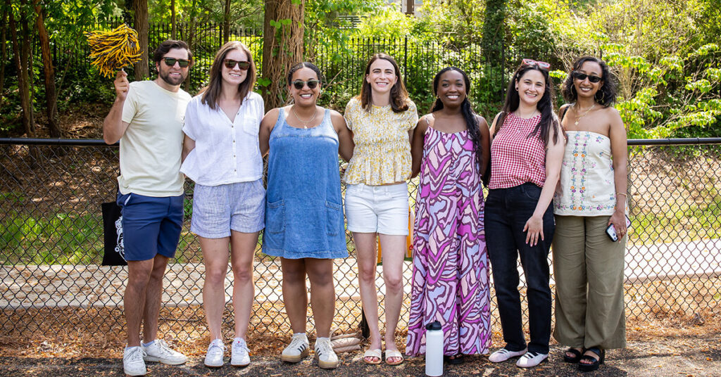 Oglethorpe Alumni stand in a line wearing sunglasses, cheering for the Petrels.