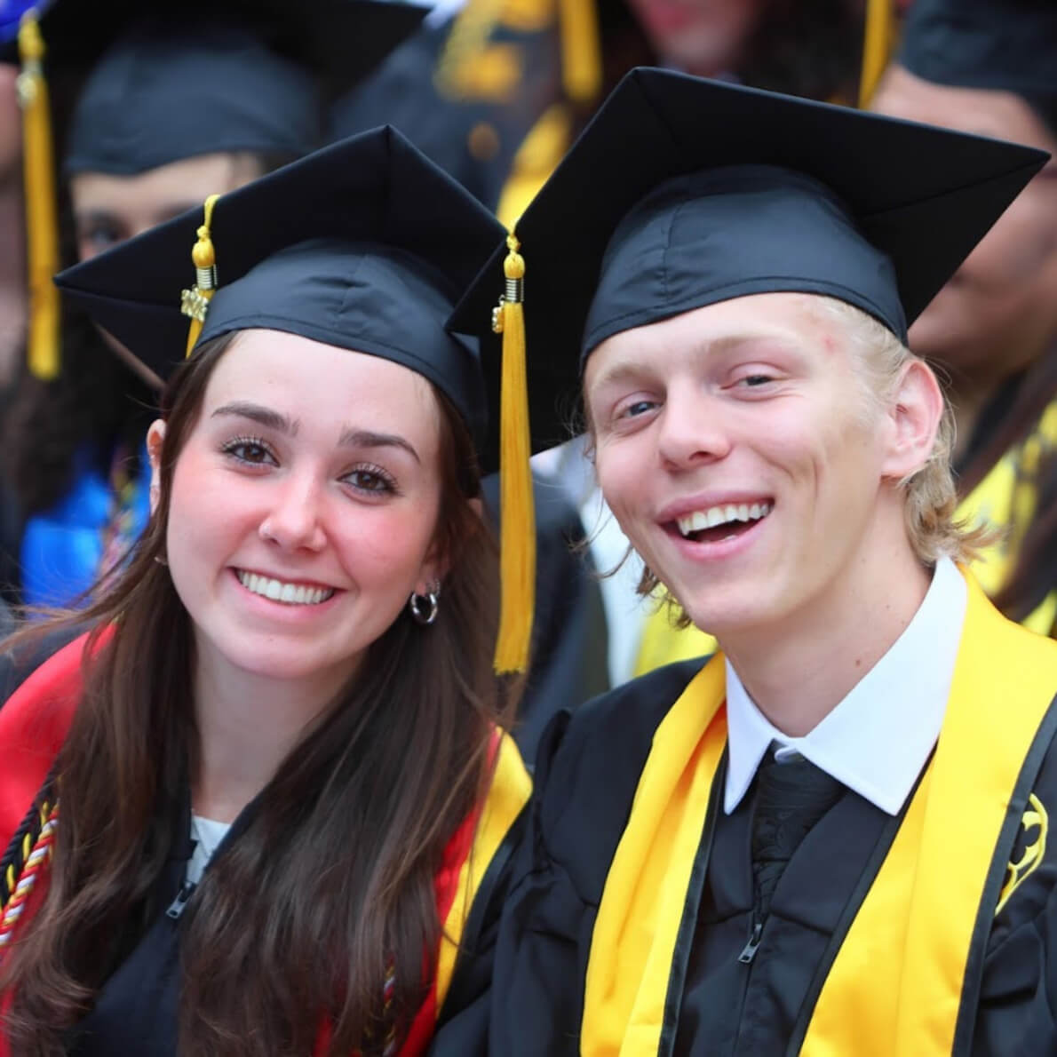 Students in their cap and gown smile during graduation ceremonies.