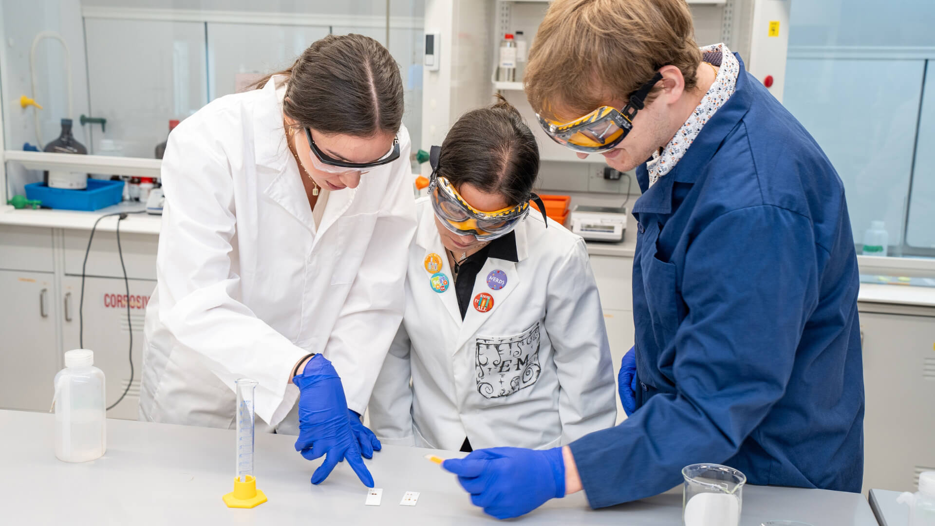 Science students wear goggles, gloves, and lab coats during an experiment.