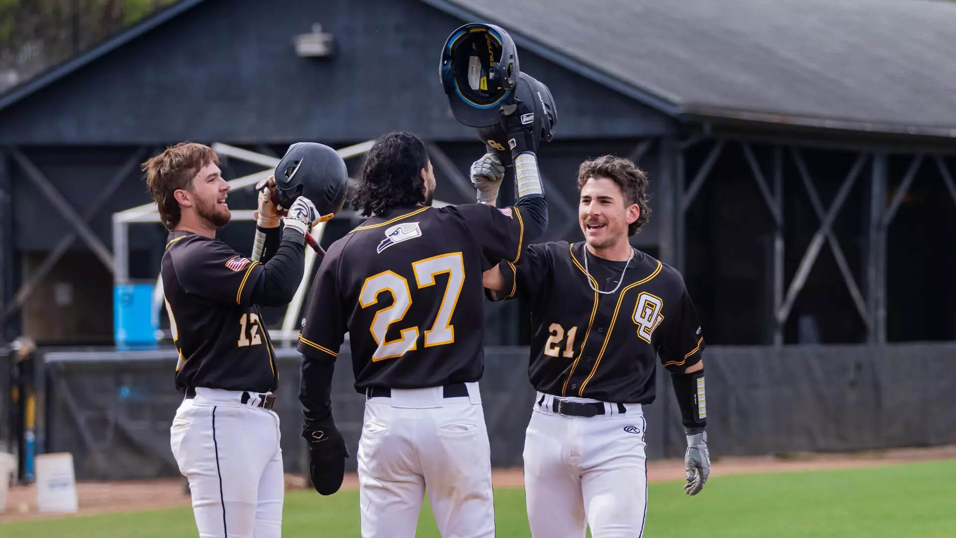 Oglethorpe University baseball players celebrate with raised helmets on the field.